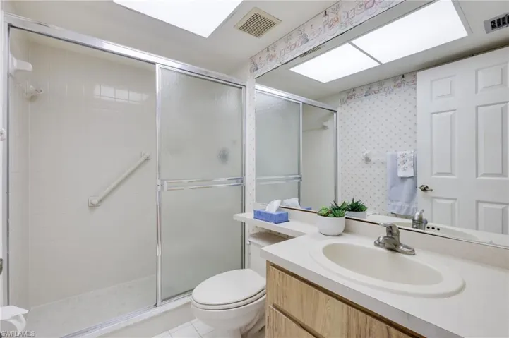 Bathroom featuring a shower with shower door, vanity with extensive cabinet space, toilet, and tile floors