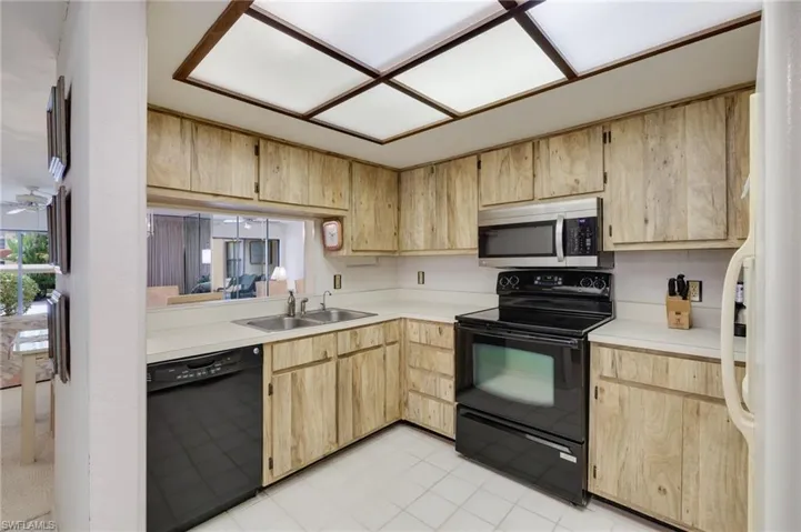 Kitchen with black appliances, sink, light tile floors, and light brown cabinets