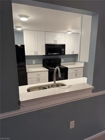 Kitchen with black appliances, white cabinets, and light stone countertops