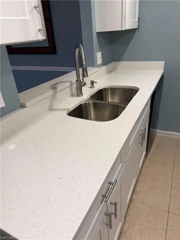 Kitchen featuring dishwashing machine, light stone countertops, white cabinets, and light tile patterned floors