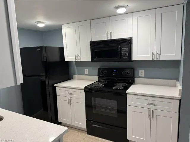 Kitchen featuring black appliances, light countertops, white cabinetry, and light tile patterned floors