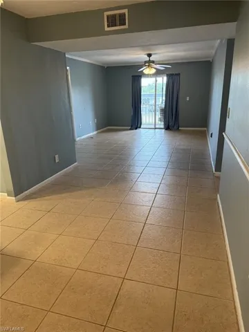 Empty room featuring ceiling fan, crown molding, and light tile patterned floors
