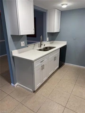 Kitchen with black dishwasher, light countertops, light tile patterned floors, and white cabinetry