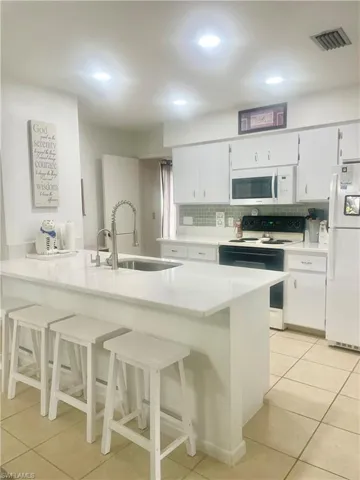 Kitchen with white appliances, light tile patterned flooring, sink, backsplash, and white cabinets