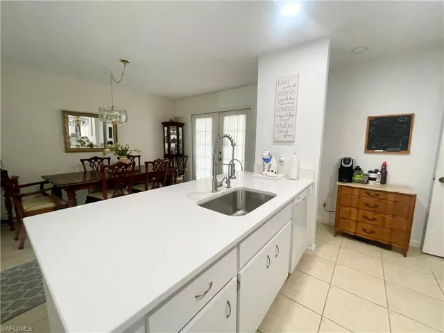 Kitchen with an island with sink, white dishwasher, white cabinetry, pendant lighting, and an inviting chandelier