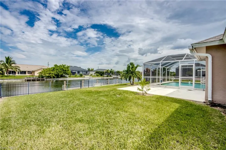 View of yard with lanai, screened in pool area, a patio area and view of dock and canal. Also features a new wrought iron fence.