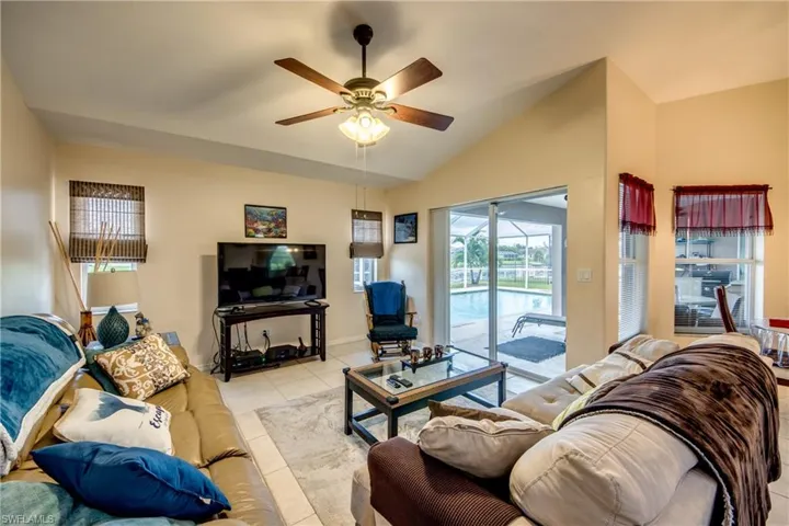 Family room with ceiling fan, continuous tile flooring, and vaulted ceiling. Sliders to pool/lanai area.
