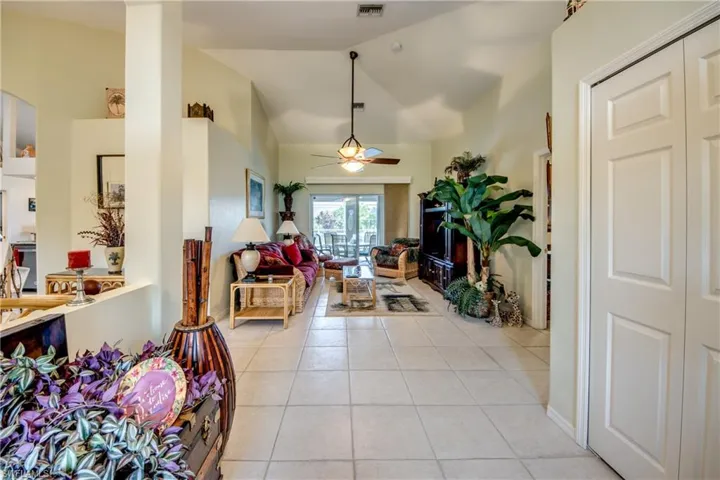 Looking in front double doors. Tiled living room featuring lofted ceiling and ceiling fan