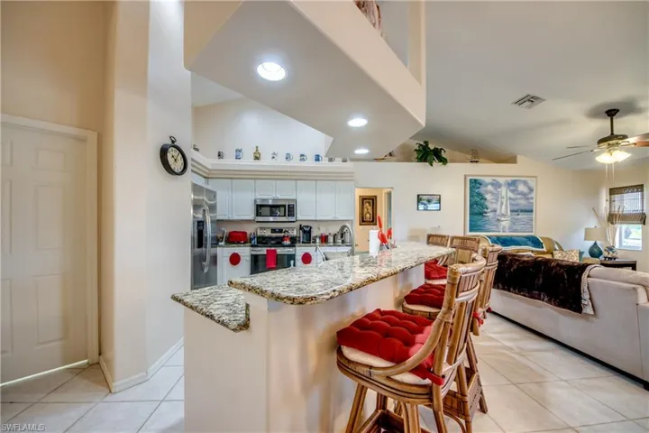 Kitchen with a breakfast bar area, white cabinetry, stainless steel appliances, granite countertops and custom ceiling feature with recessed lights.