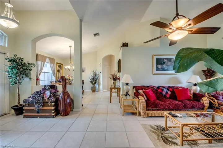 Looking in to tiled living room on right featuring ceiling fan with notable chandelier and lofted ceiling