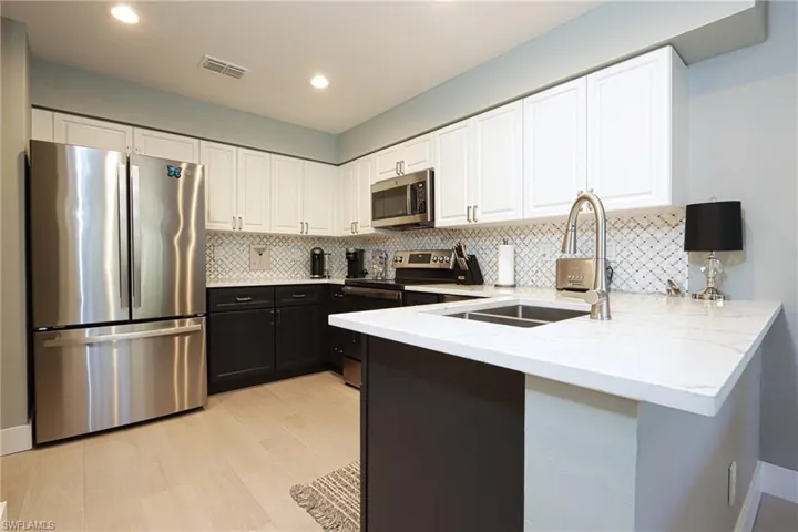 Kitchen featuring appliances with stainless steel finishes, a sink, a peninsula, light stone countertops, and white cabinetry