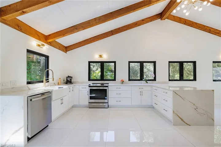 Kitchen with white cabinetry, light stone counters, stainless steel appliances, a peninsula, and high vaulted ceiling