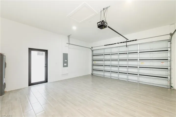 Garage featuring electric panel, a garage door opener, and water heater