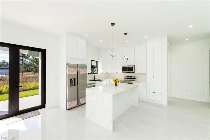 Kitchen featuring appliances with stainless steel finishes, french doors, white cabinetry, a kitchen island, and decorative light fixtures