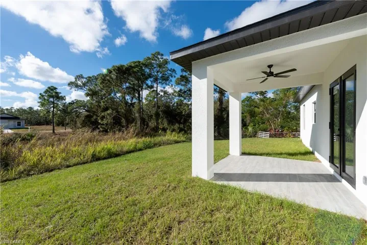 View of grassy yard featuring a ceiling fan, a patio area, and view of scattered trees