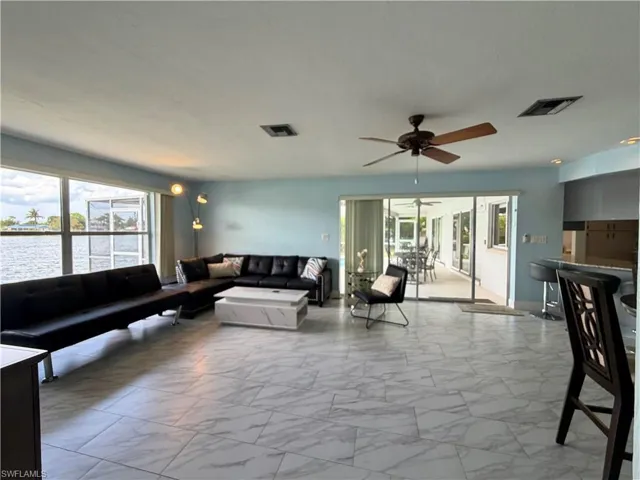 Bright living space featuring large windows, water frontage, and wood-finish ceiling fan