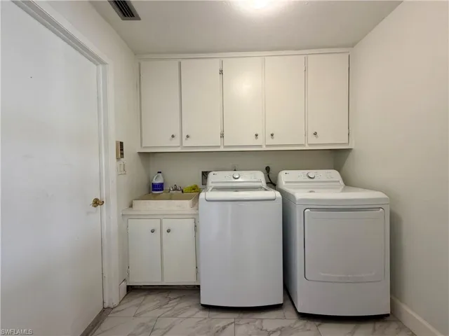 Utility room featuring white shaker-style cabinetry, a utility sink with base storage, and marble-look tile flooring