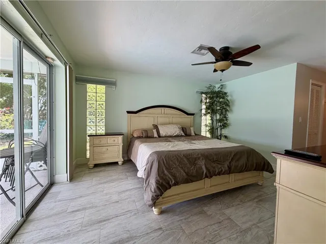 Sliding glass doors opening to outdoor living, light-toned walls, ceiling fan, glass block window, and tile flooring