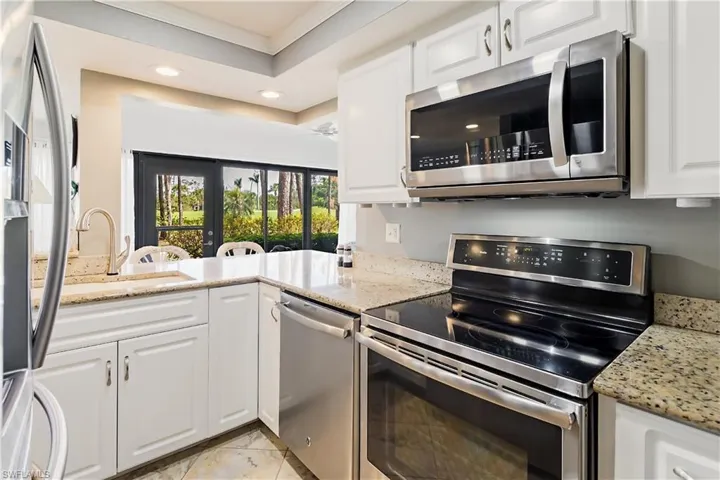 Kitchen with stainless steel appliances, white cabinetry, sink, and light stone counters