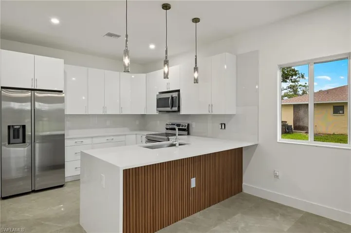Kitchen with stainless steel appliances, kitchen peninsula, hanging light fixtures, and white cabinets