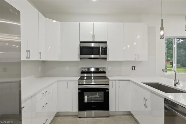 Kitchen featuring stainless steel appliances, hanging light fixtures, sink, and white cabinetry