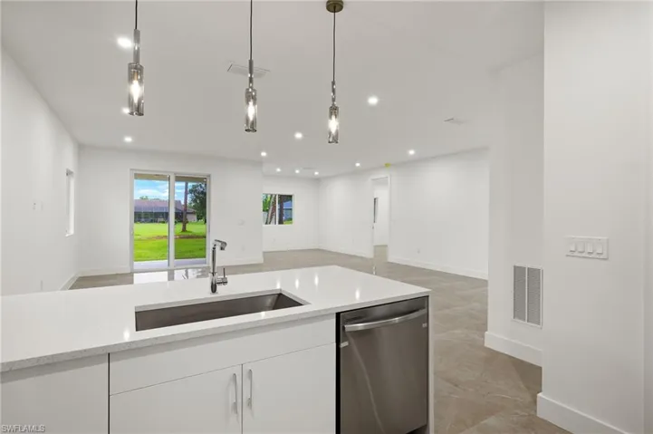 Kitchen with sink, light stone counters, dishwasher, hanging light fixtures, and white cabinets