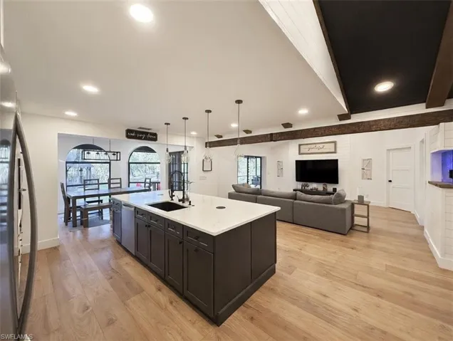 Kitchen with open floor plan, light wood-style floors, a center island with sink, stainless steel appliances, and decorative light fixtures