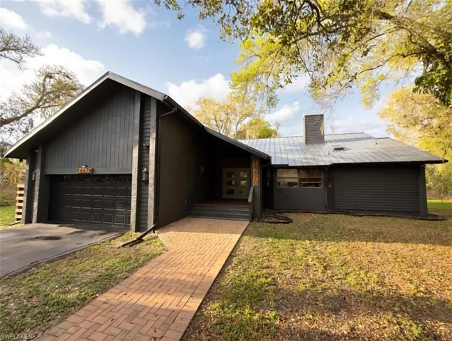 View of front facade with a chimney, a garage, driveway, and a front lawn