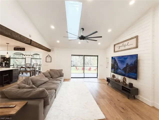 Living area featuring a skylight, vaulted ceiling, light wood finished floors, ceiling fan, and healthy amount of natural light