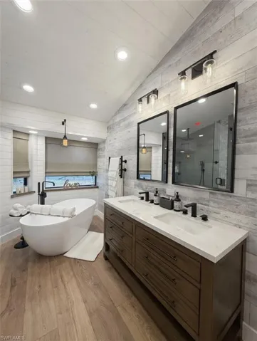 Full bath with lofted ceiling, double vanity, light wood-style flooring, a soaking tub, and a stall shower