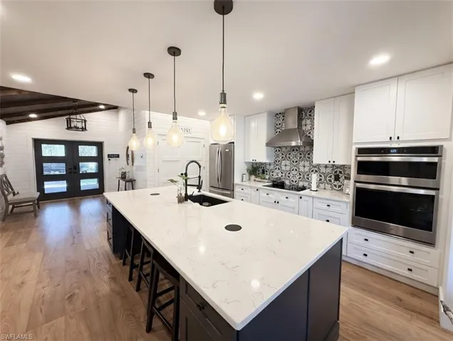 Kitchen with light wood-style flooring, a kitchen bar, a large island, french doors, and dual tone cabinetry