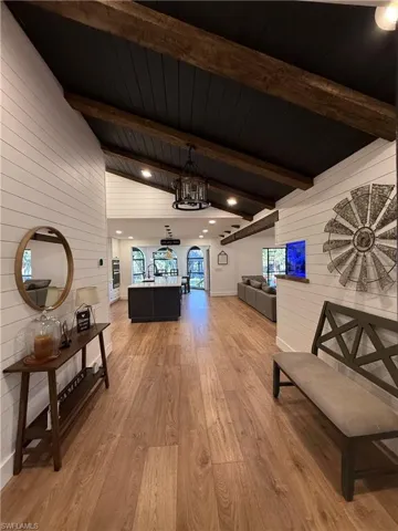 Corridor with wood walls, light wood-type flooring, and lofted ceiling