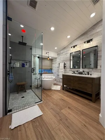 Full bath featuring vaulted ceiling, double vanity, a stall shower, a freestanding bath, and recessed lighting