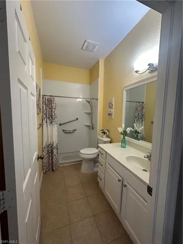 Bathroom featuring a shower with curtain, vanity, tile patterned flooring, and toilet