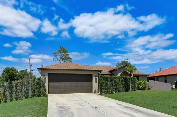 Single-story residence featuring a two-car garage with a paneled door, concrete driveway, and mature shrubbery