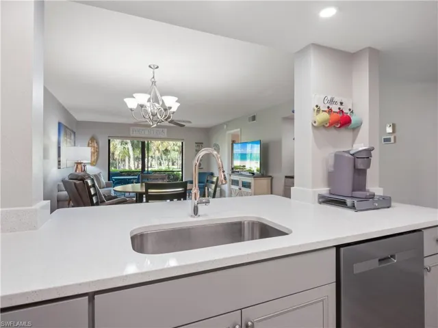 Kitchen with a sink, pendant lighting, stainless steel dishwasher, open floor plan, and an inviting chandelier