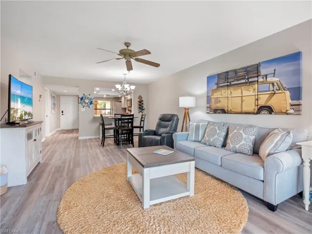 Living room featuring baseboards, light wood-style flooring, and ceiling fan with notable chandelier