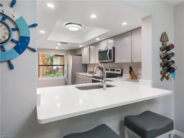 Kitchen with a raised ceiling, a peninsula, appliances with stainless steel finishes, and a breakfast bar