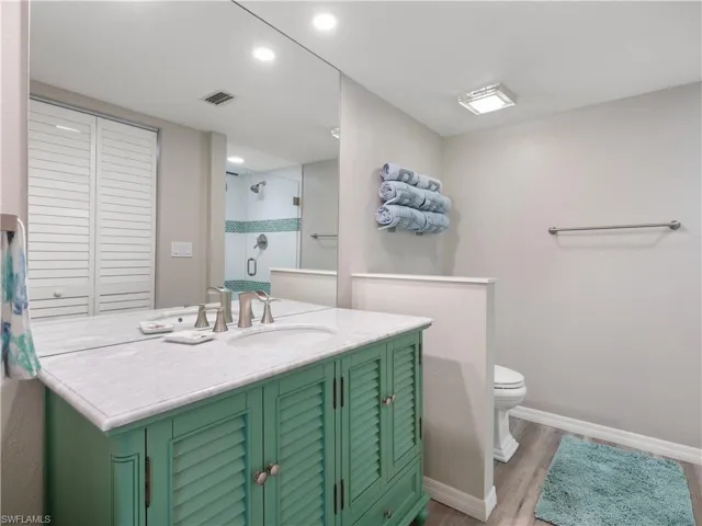 Bathroom with toilet, a stall shower, baseboards, and wood finished floors