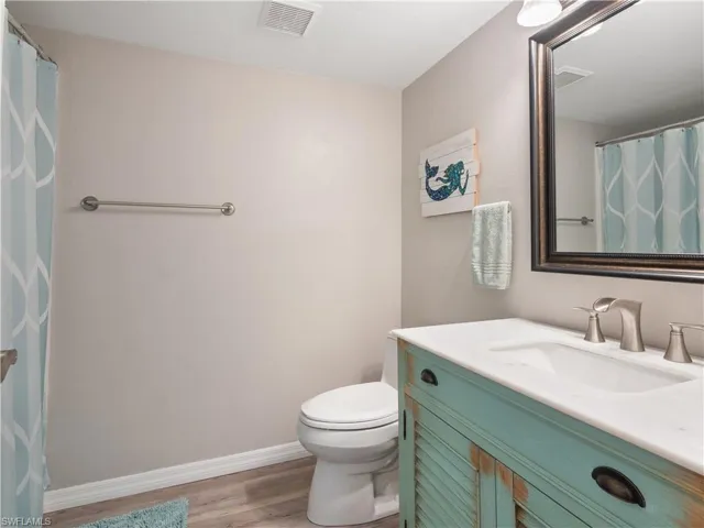 Bathroom featuring vanity, toilet, baseboards, visible vents, and wood finished floors