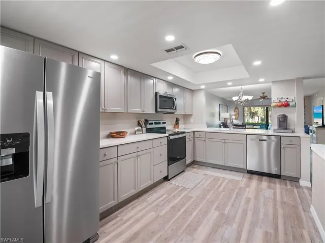 Kitchen with gray cabinets, a raised ceiling, stainless steel appliances, visible vents, and an inviting chandelier