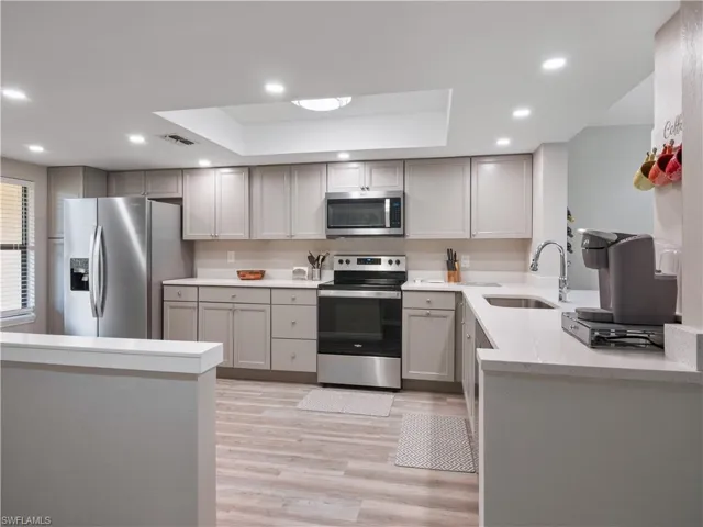 Kitchen featuring gray cabinetry, a raised ceiling, a sink, and appliances with stainless steel finishes