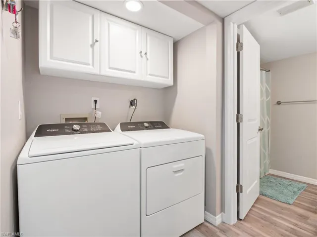 Washroom with light wood finished floors, washing machine and clothes dryer, baseboards, visible vents, and cabinet space