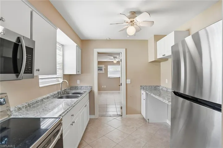 Kitchen with stainless steel appliances, white cabinets, ceiling fan, light tile patterned floors, and light stone counters