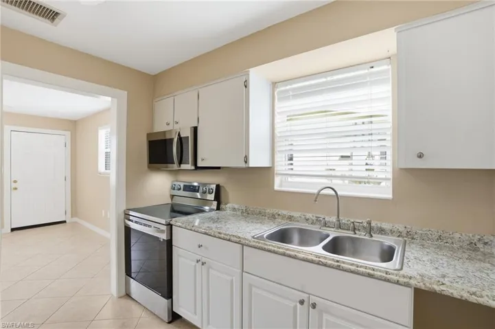 Kitchen with stainless steel appliances, light countertops, white cabinets, and light tile patterned flooring