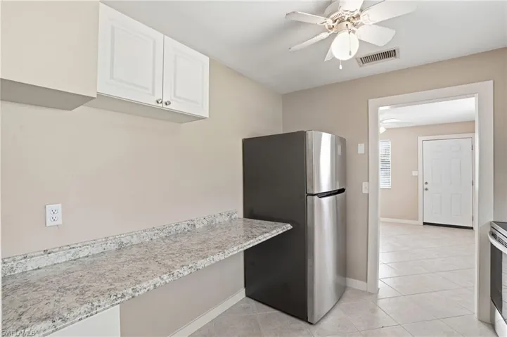 Kitchen featuring stainless steel appliances, ceiling fan, light tile patterned floors, white cabinetry, and light stone counters
