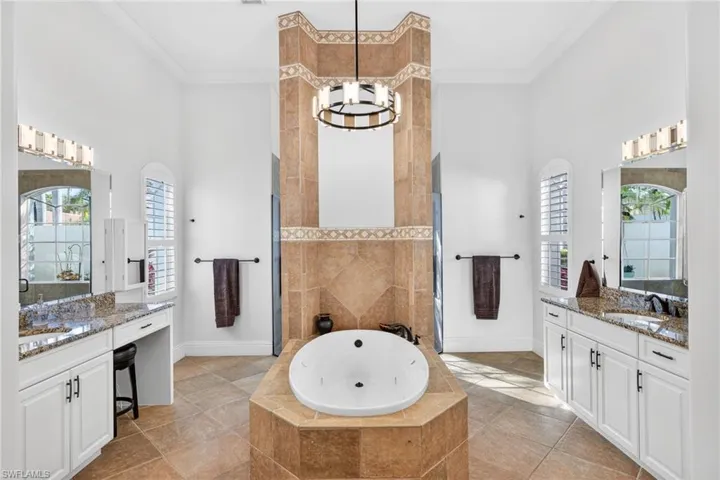 Bathroom featuring a high ceiling, two vanities, a whirlpool tub, walk in shower, and ornamental molding