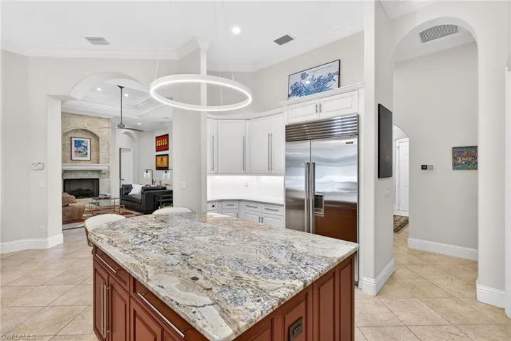 Kitchen featuring arched walkways, pendant lighting, light stone countertops, built in refrigerator, and open floor plan