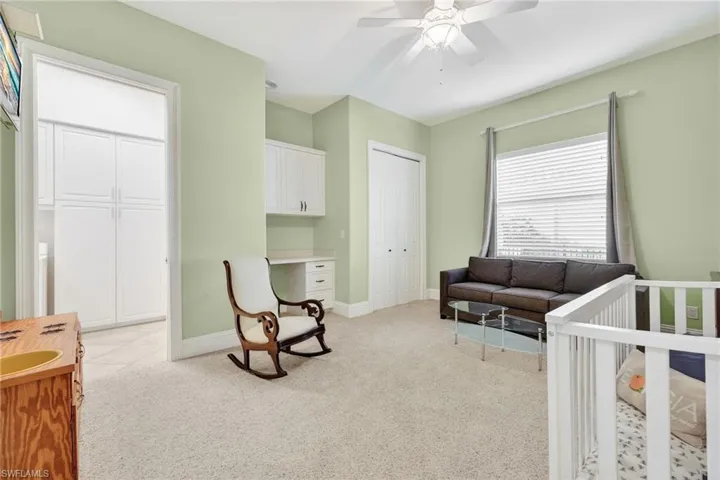 Bedroom with a nursery area, built in desk, light colored carpet, and ceiling fan