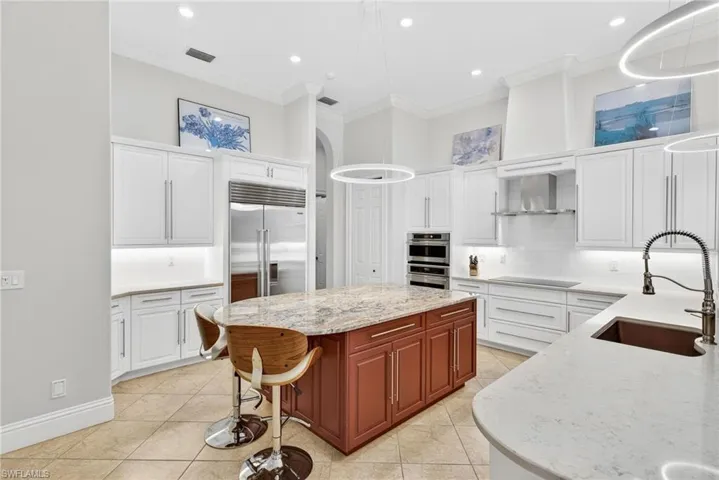 Dual tone kitchen with ornamental molding, light stone countertops, decorative backsplash, a center island, and stainless steel appliances